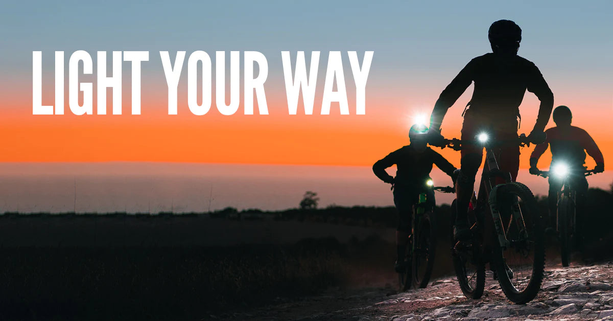 3 people on bicycles with a sunset in the background. The words Light Your Way appear in the sky