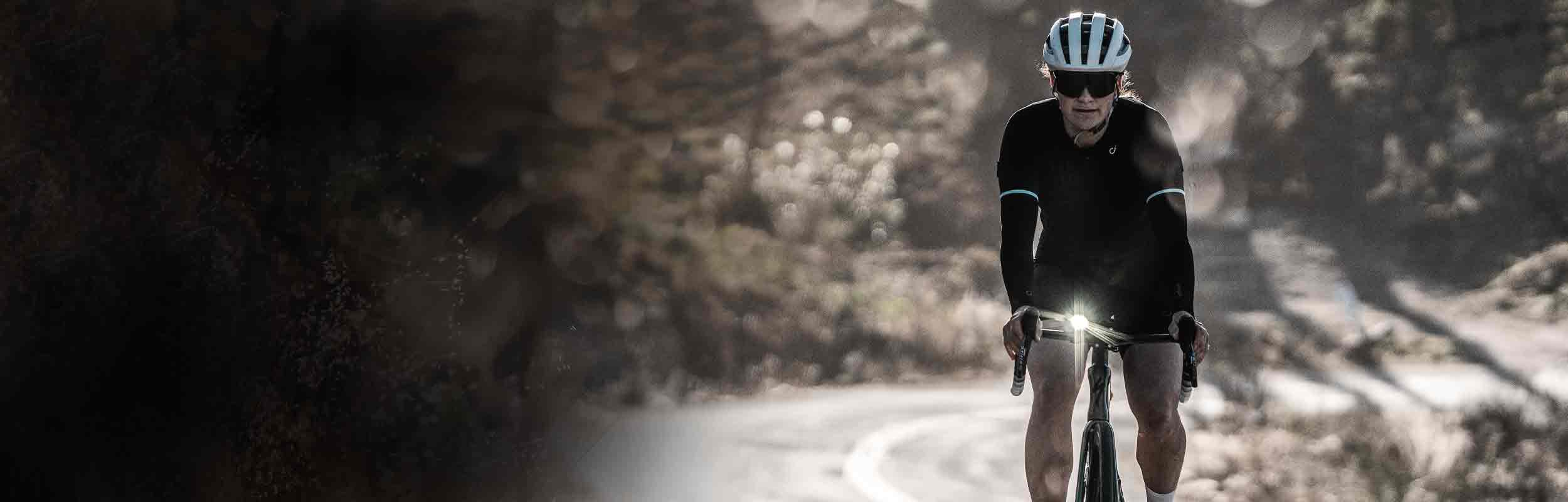 A person riding a bicycle on a road with a bright front light mounted on the handlebars.