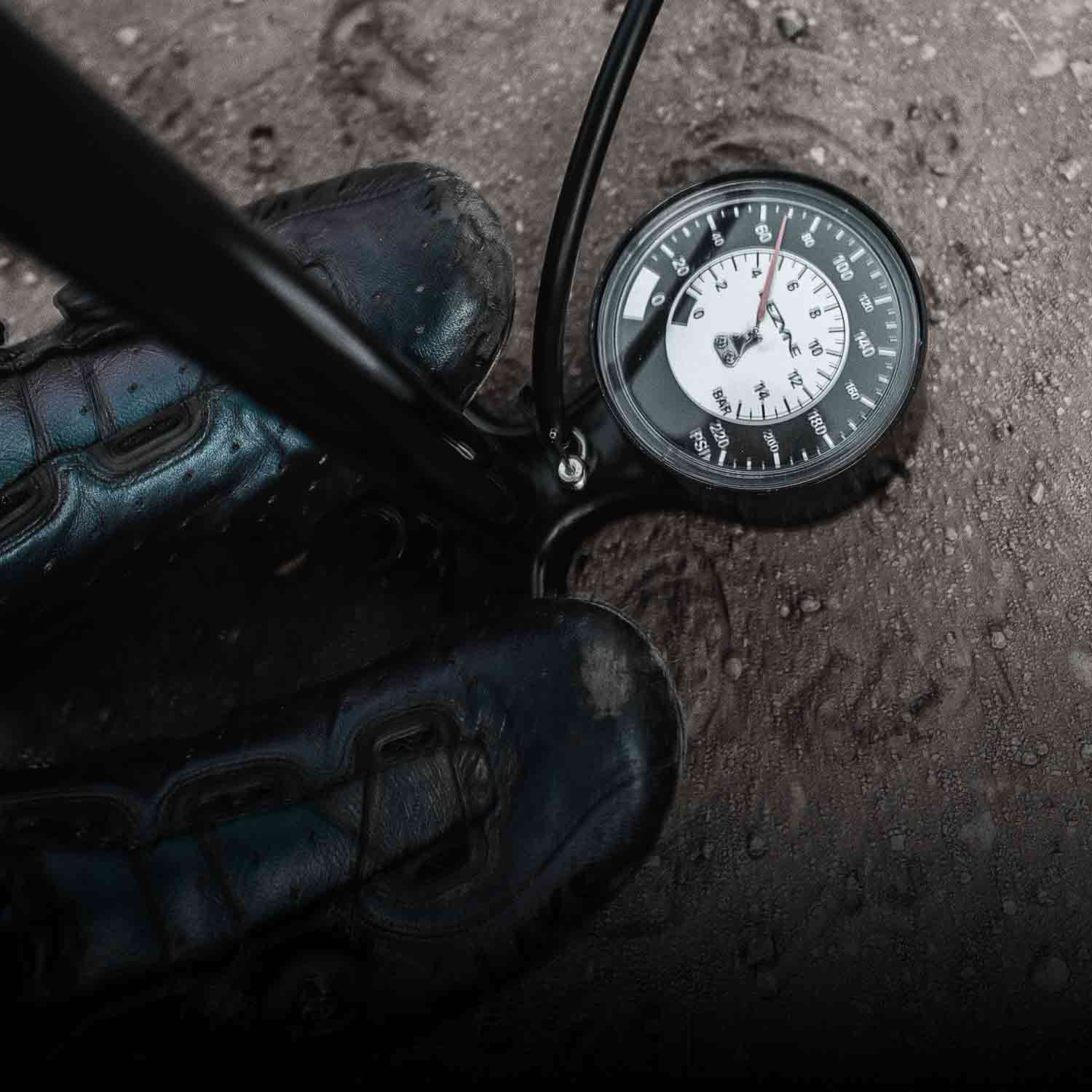 Someones feet on the base of a bicycle floor pump with an analog pressure gage.