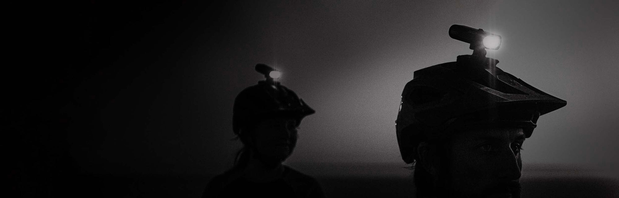 2 bicycle helmet lights mounted on helmet that people are wearing on a dark background.