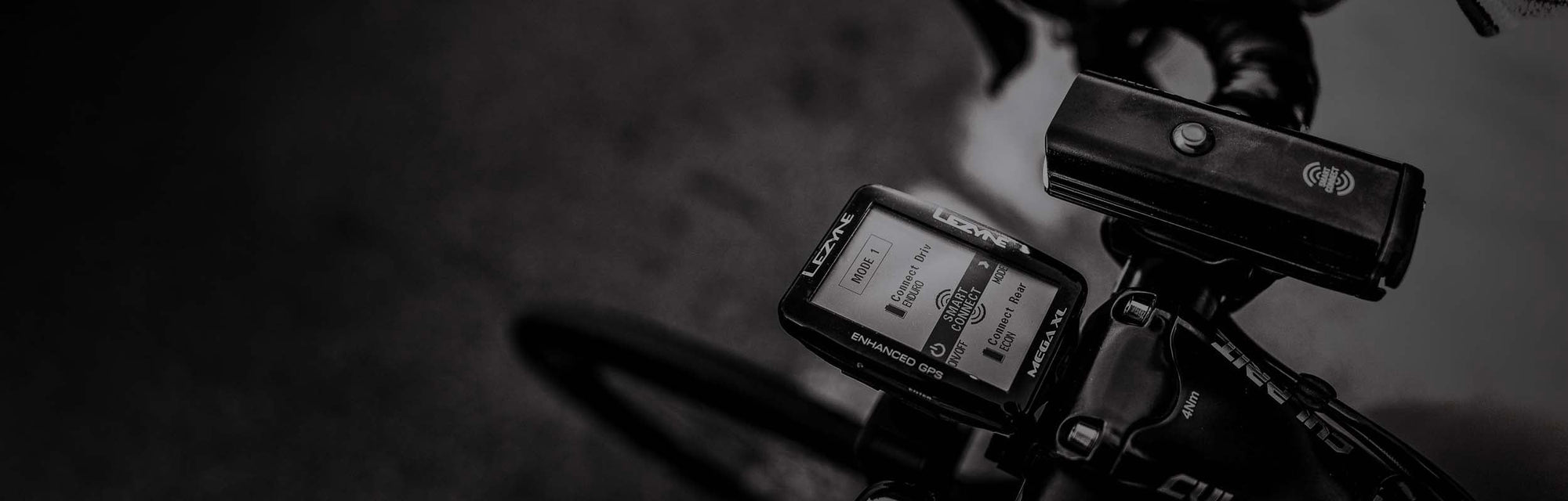 A GPS computer and a light with the words smart connect printed on it mounted to a bicycles handlebars.