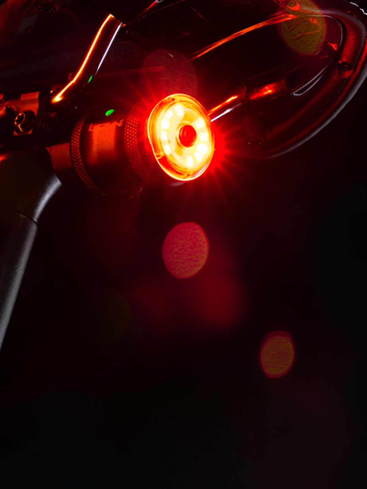 Close-up of the Lezyne Saddle AI Alert 250 bright red glowing LED rear light mounted on the black seat post of a road bike