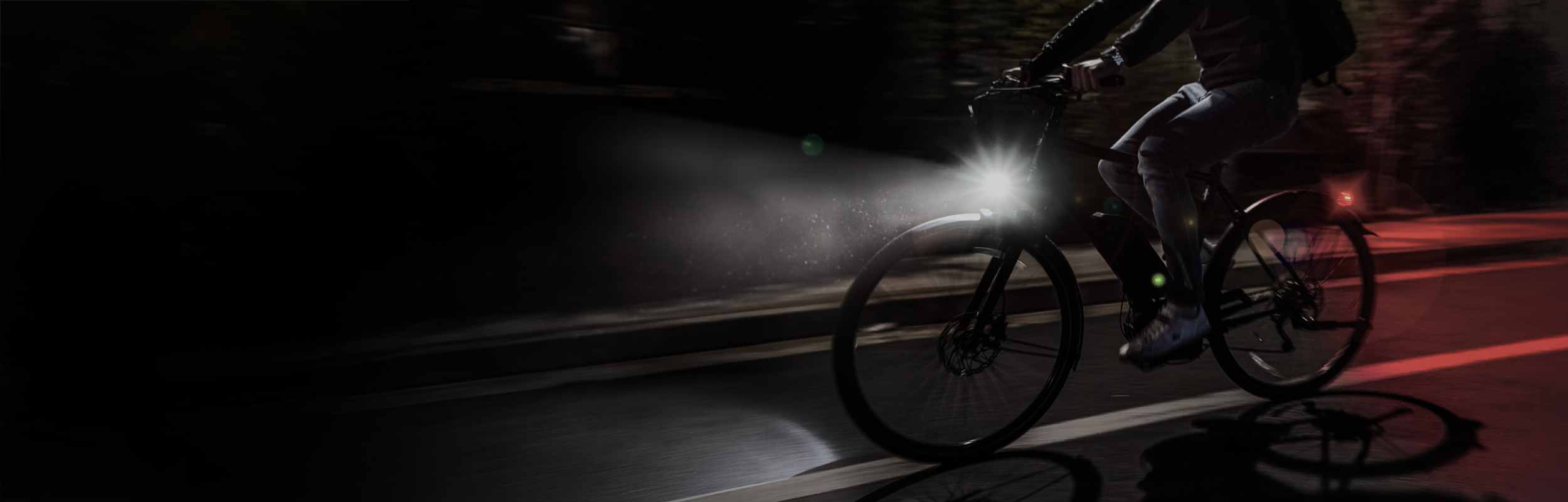 An e-bike that appears to be moving quickly on a road being ridden at night with a front light and a rear light mounted on the bike.