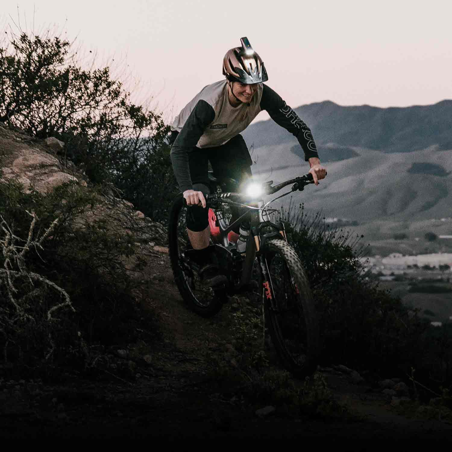 Someone riding a mountain bike on steep terrain with a bright front light on the handlebars.