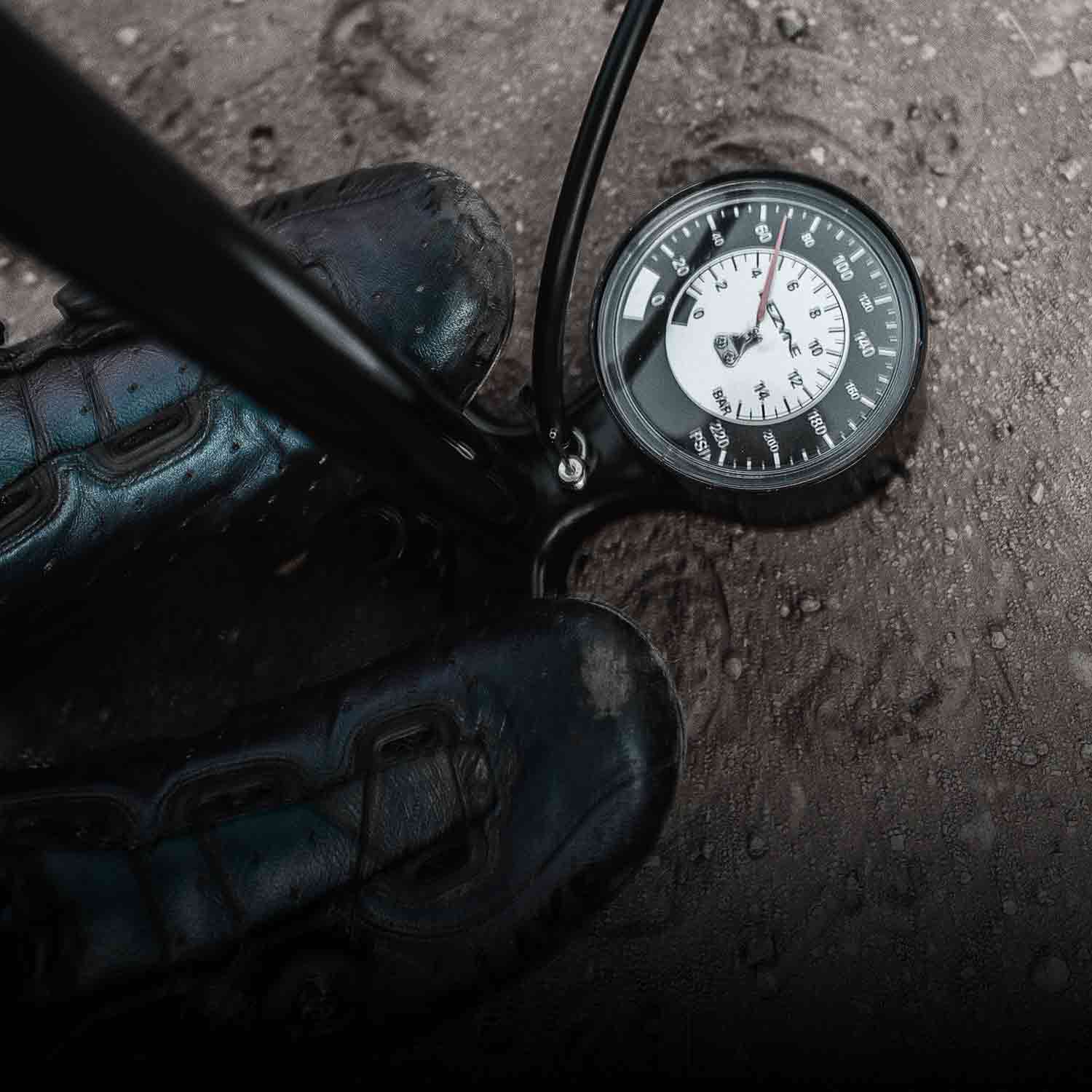 Someones feet on the base of a bicycle floor pump with an analog pressure gage. 