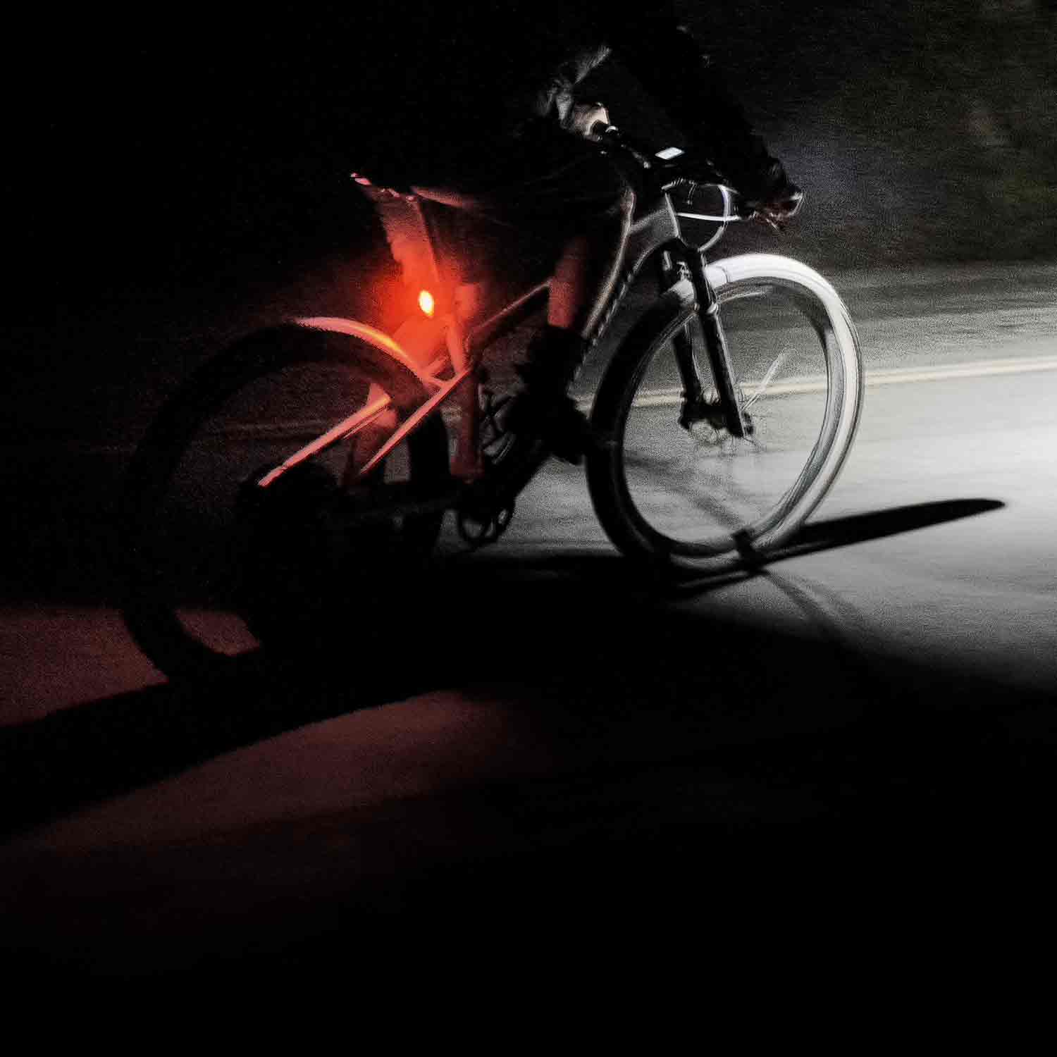 A side view of someone riding on a very dark road with a red rear light a a bright front light.
