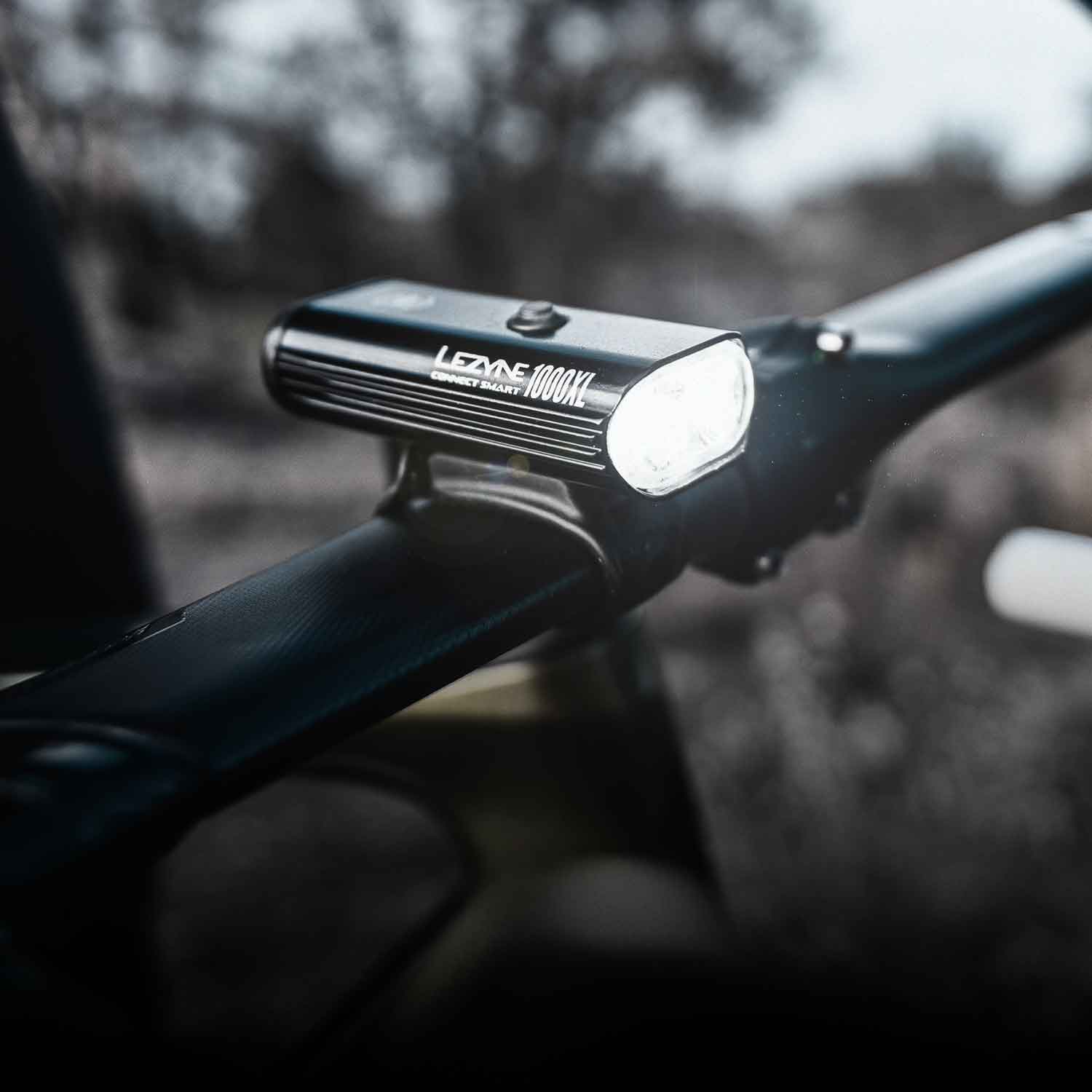 A bright front light mounted on bicycle handlebars with the words Lezyne 1000XL Connect Smart printed on the side of the light.