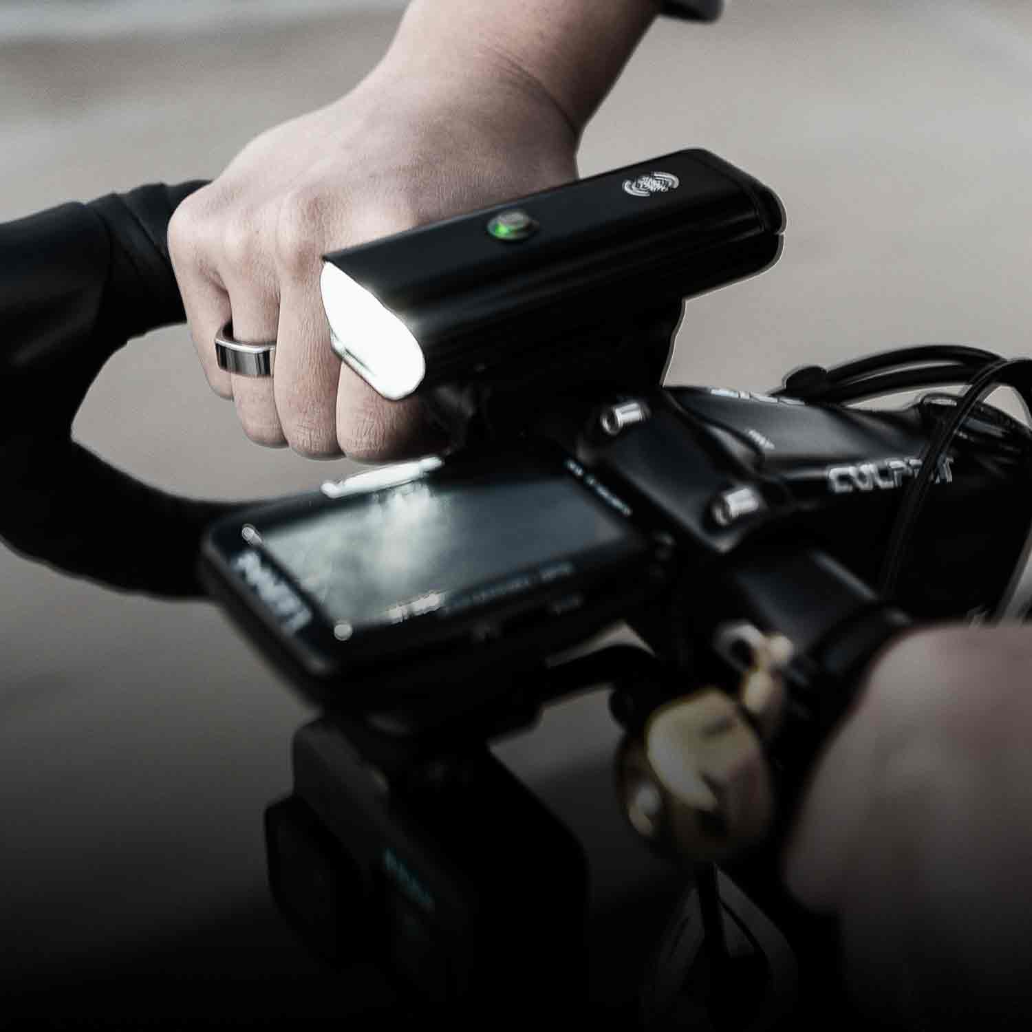 Hands on bicycle handlebars with a GPS computer and a bright front lite mounted to it.