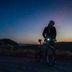 Lezyne Radar React System lifestyle scene; cyclist at road bike at dusk adjusting lights before ride, evening sky in background.